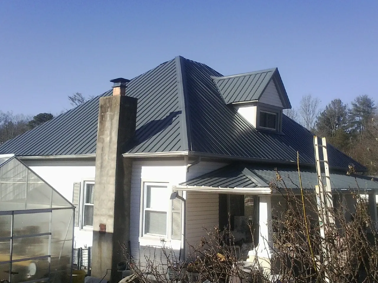 Dark blue standing seam metal roof on a white farmhouse with dormer — Slate & Tile Roof Repair by Roofing Brothers in Rose