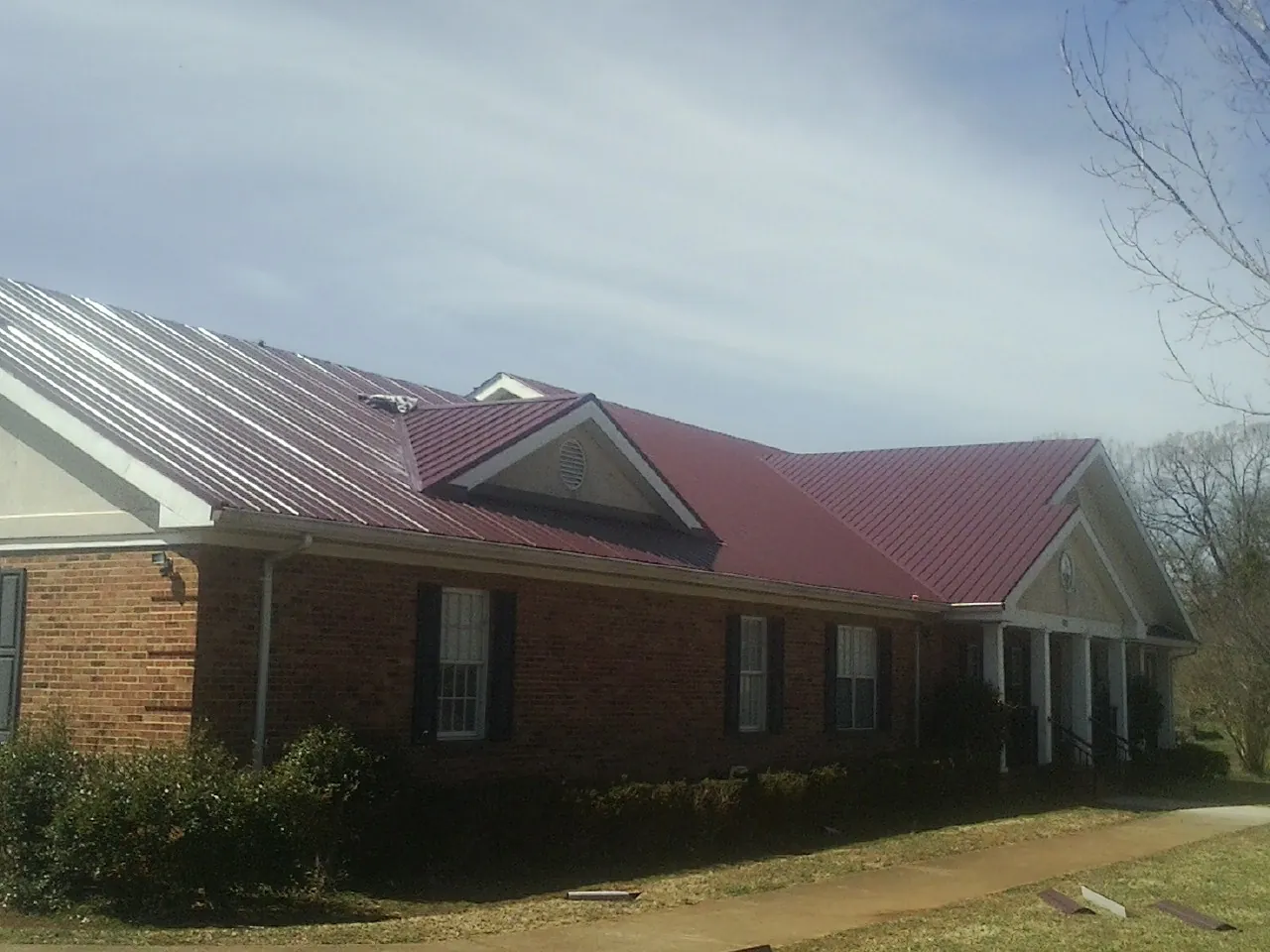 Red metal roof with gabled entries on a long brick building, from a Hail Damage Roof Repair job in Rose