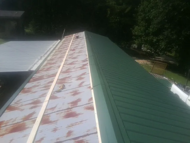 Old rusted panels beside newly installed green metal roofing — Wind Damage Roof Repair by Roofing Brothers in Rose