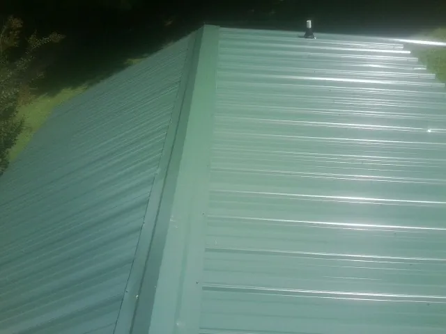 New green metal panels meeting at the ridge of a roof — Flat Roof Repair work by our crew in Rose