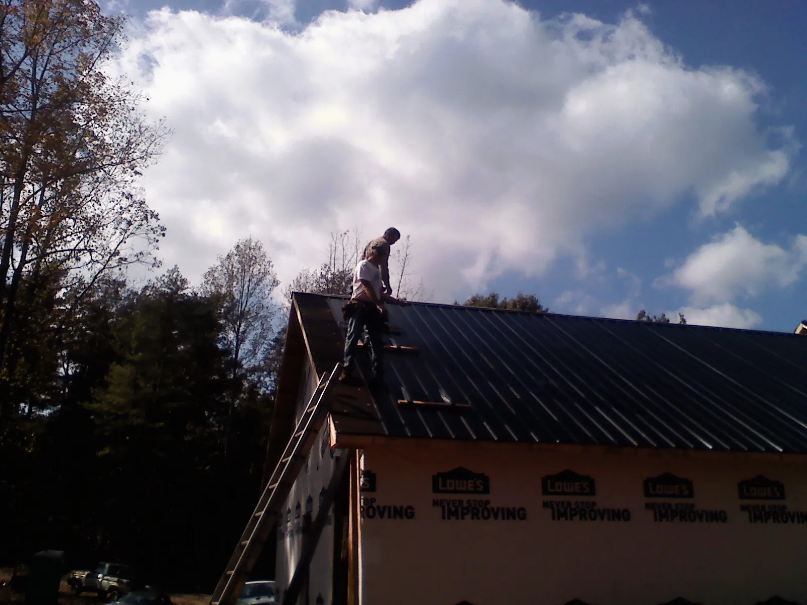Roofer fastening dark metal panels high against a cloudy sky, from a Roof Inspection job in Rose