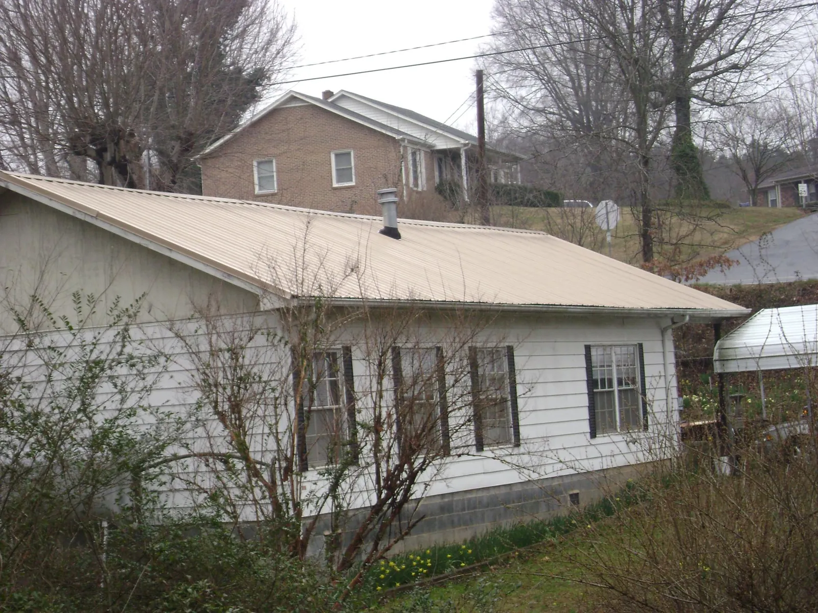 Tan metal roof on a white sided house set into a hillside — Commercial Roofing by Roofing Brothers in Rose