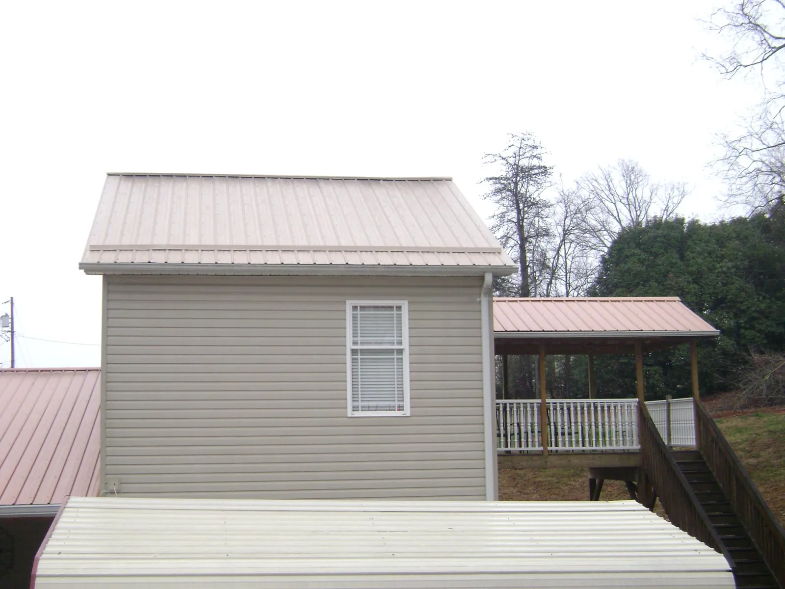 Tan metal roofs on a two story addition and attached porch, from a Roof Replacement job in Rose